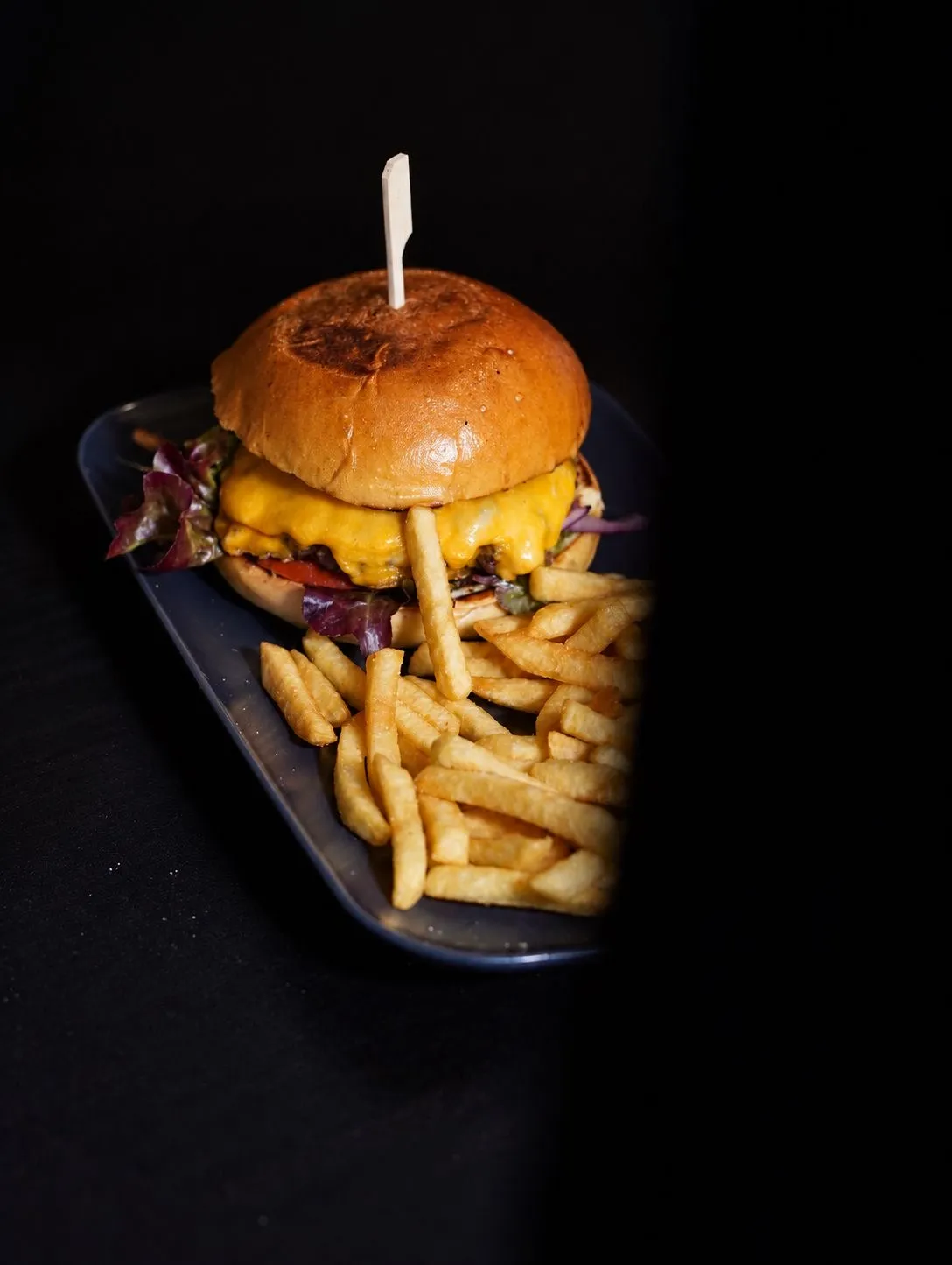 Burger mit Käse und Pommes auf dunklem Teller