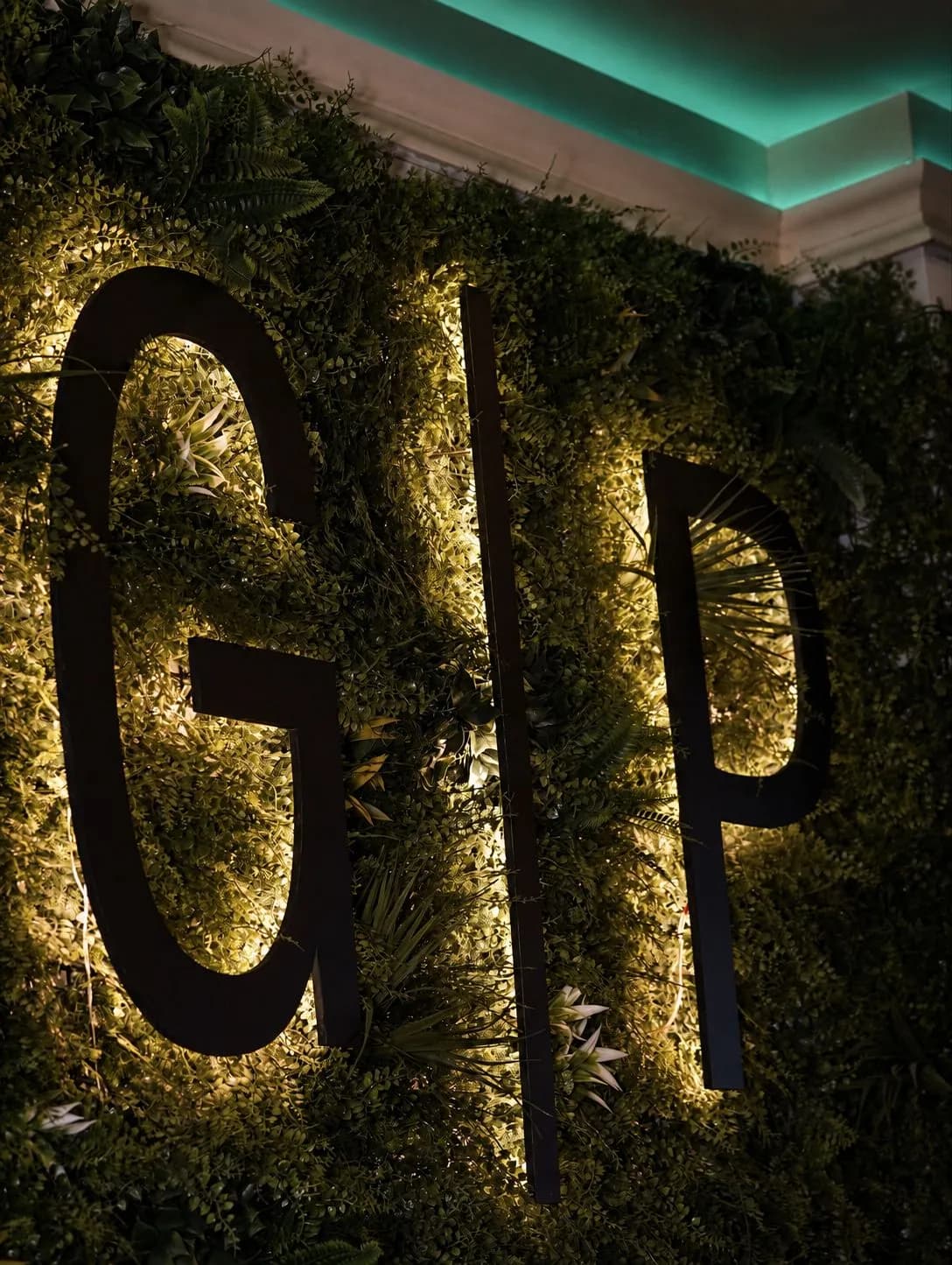Beleuchtetes GP-Logo an der begrünten Wand im Lokal der Goldenen Panade