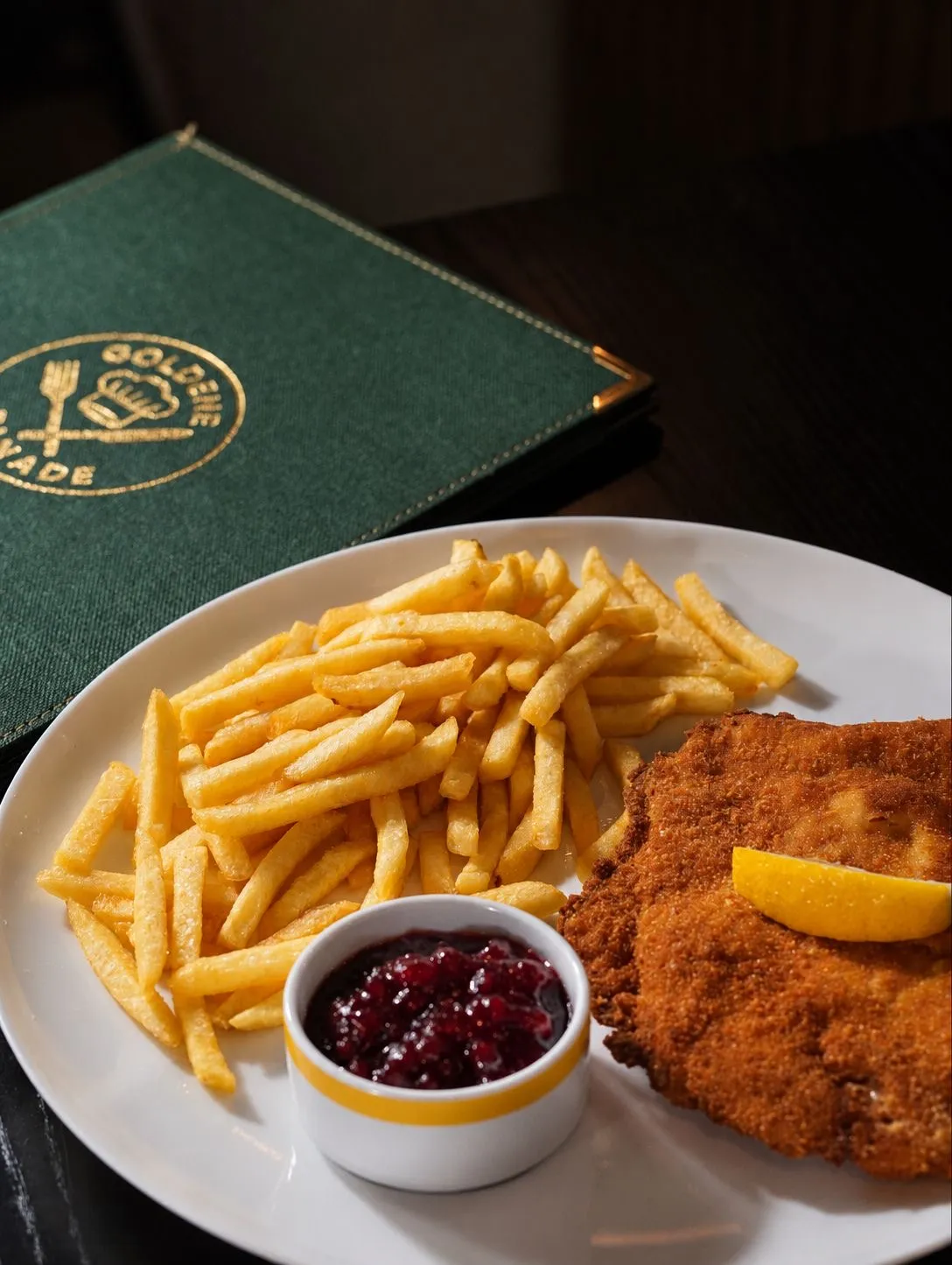 Schnitzel mit Pommes und Preiselbeeren vor der grünen Speisekarte der Goldenen Panade
